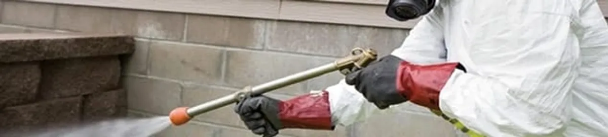 Pest control technician applying exterior insect treatment along a home foundation in Jacksonville, FL