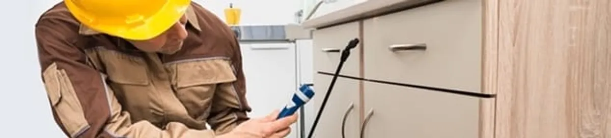 Roach exterminator applying treatment under kitchen cabinets in Jacksonville, FL