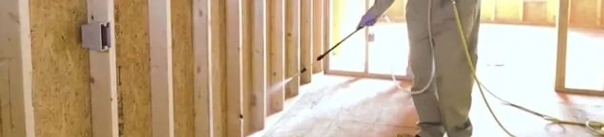 Termite treatment technician applying spray along framing and unfinished walls in Jacksonville, FL
